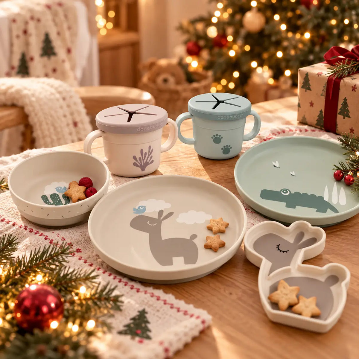 Pratos, taças e copos infantis Done by Deer numa mesa com decoração de Natal delicada.